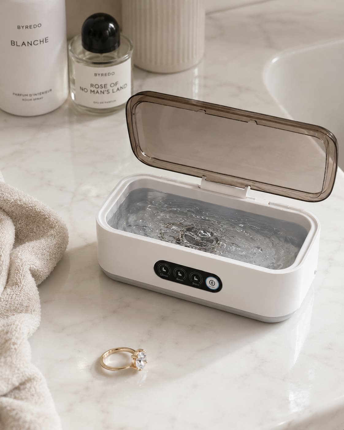 Aurelle Sparkle Bath ultrasonic jewelry cleaner open on a marble vanity with a diamond ring beside it